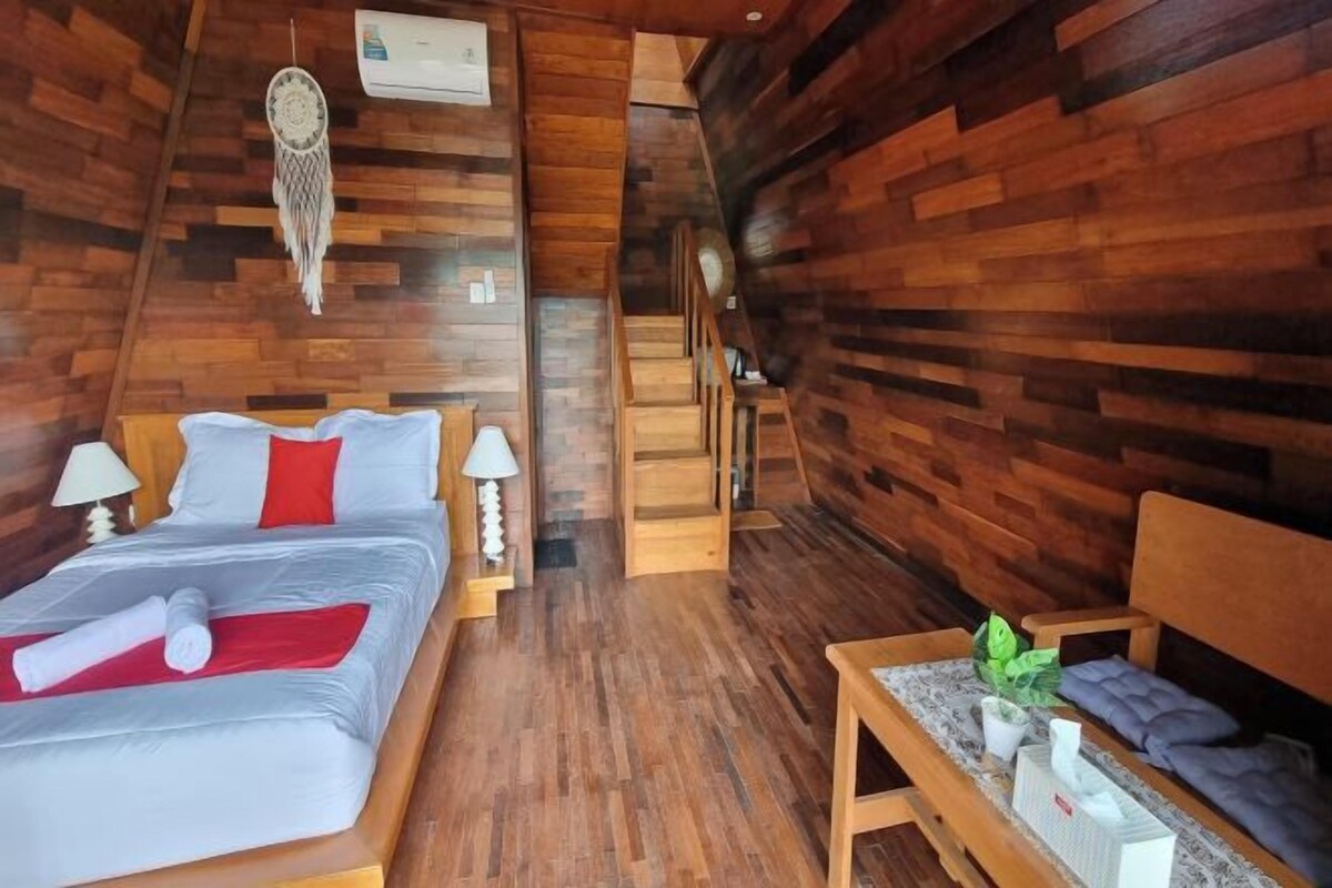 Una habitación de madera con una cama, mesitas de noche y un banco.