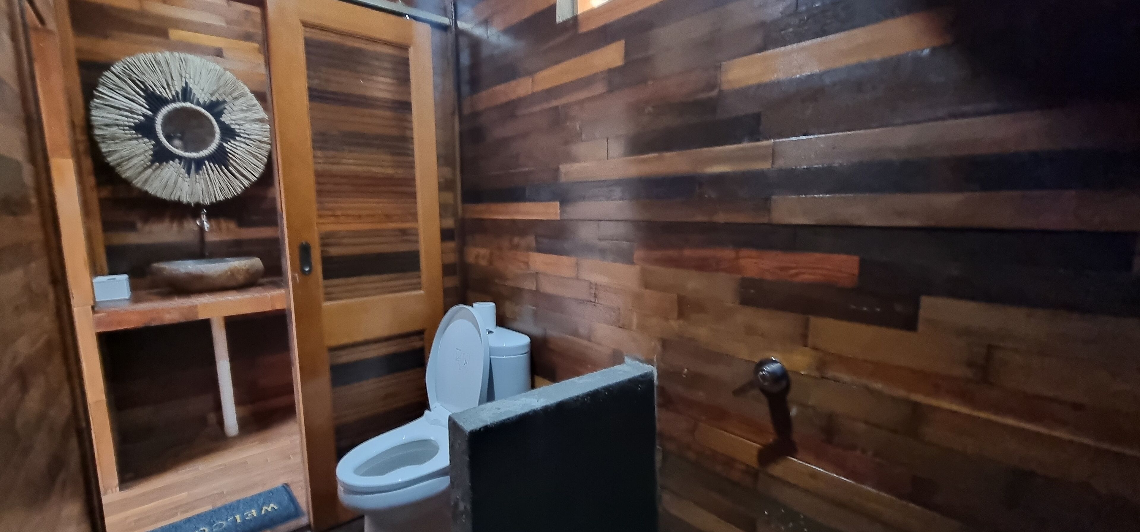 Un baño con paneles de madera, un inodoro, un adorno en la pared y un pequeño estante.