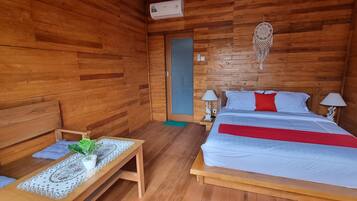 Una habitación de madera con una cama, mesitas de noche, una pequeña mesa con una planta y un atrapasueños en la pared.