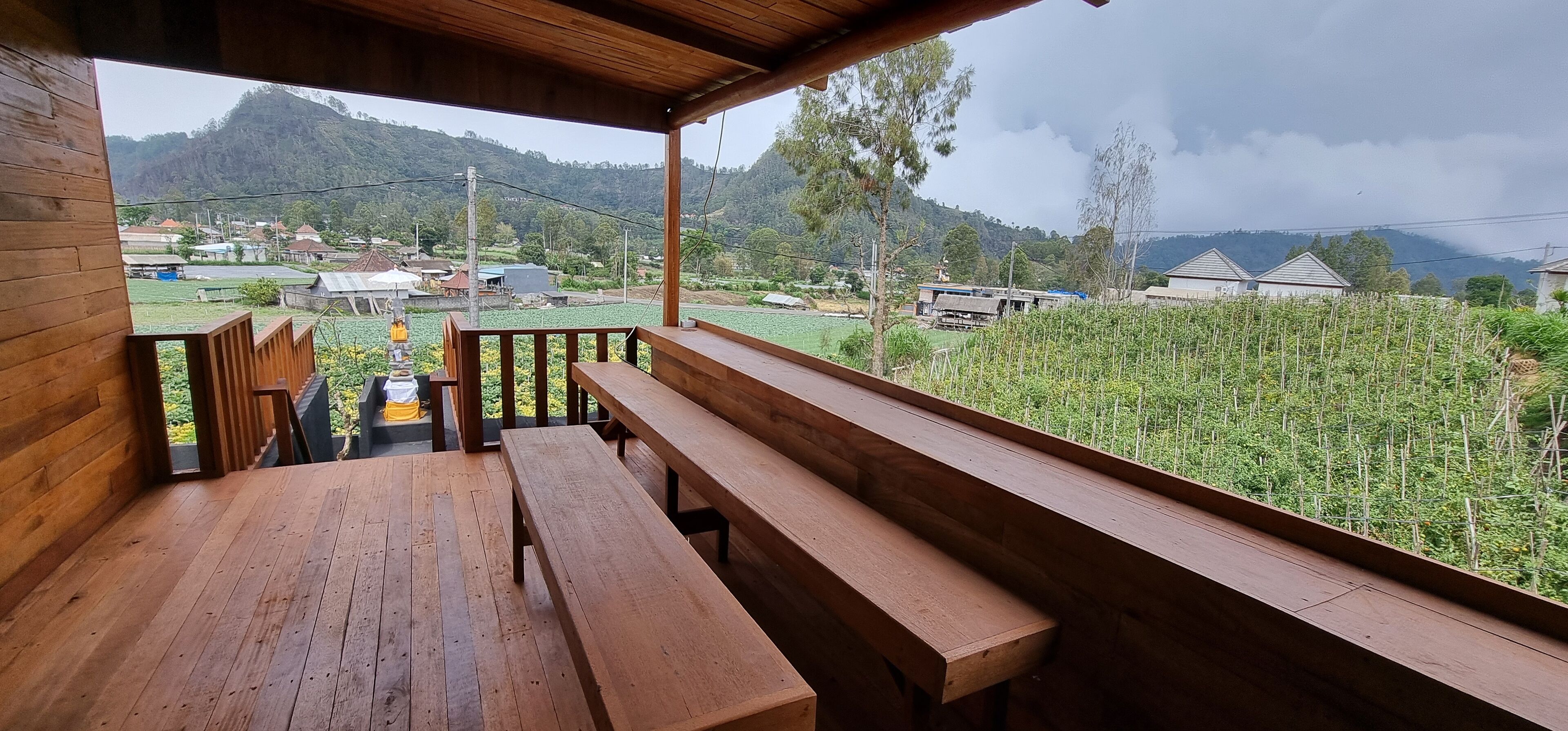 Una terraza de madera con bancos que da a un paisaje rural con campos y casas.