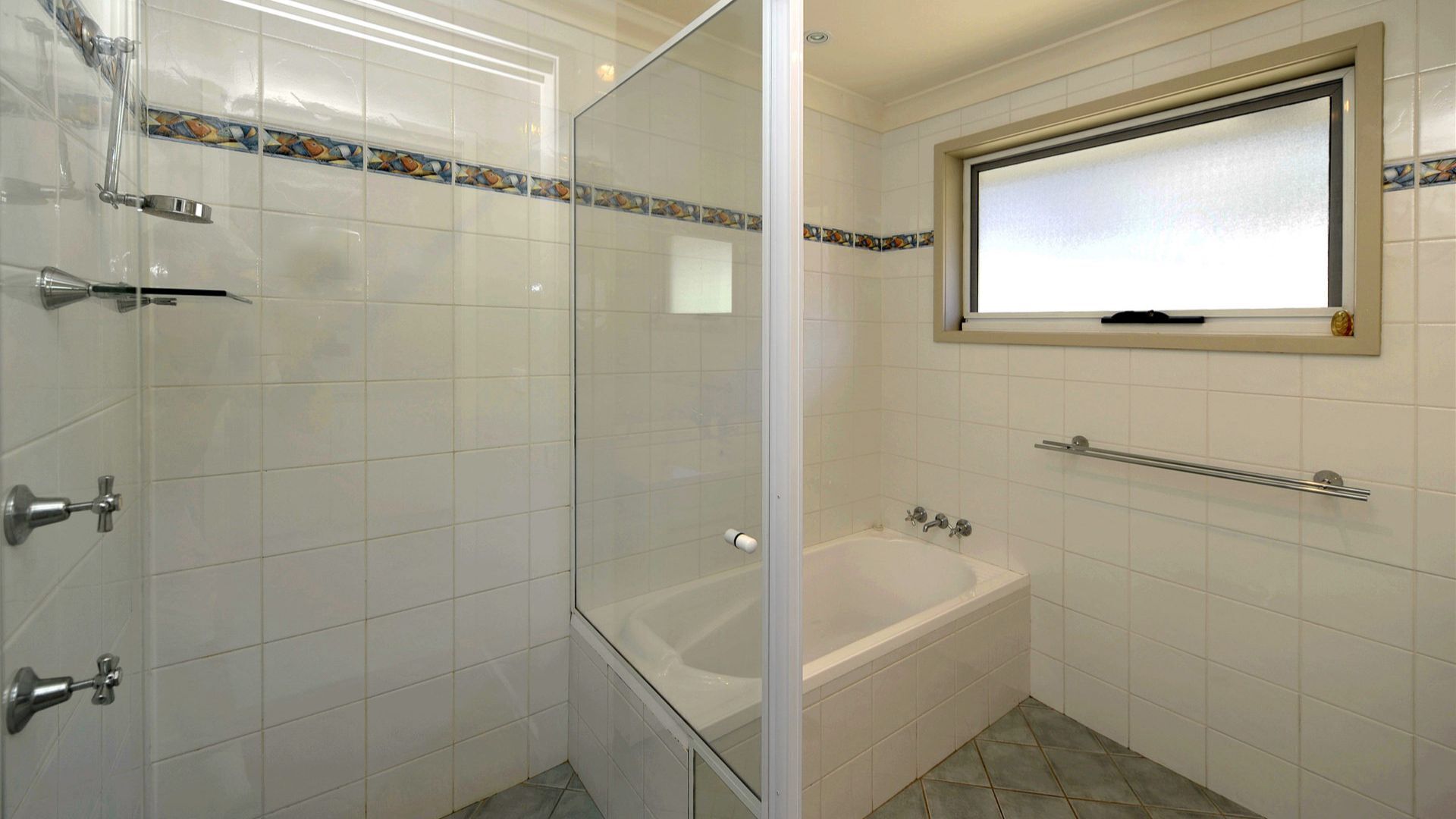 Une salle de bain avec des carreaux blancs, une douche en verre, une baignoire et une fenêtre en verre dépoli.