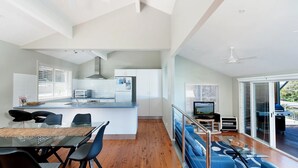 Une cuisine moderne dotée d’un îlot central, un coin repas avec une table en verre et un salon avec un canapé bleu et un téléviseur.
