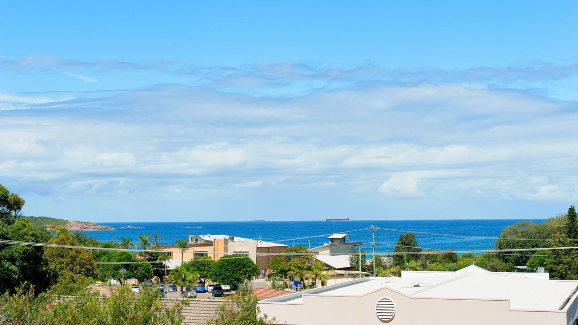 A coastal town with buildings overlooking the sea, a clear sky, and a distant ship.