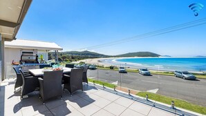 Un balcon avec une table et des chaises, donnant sur une plage et l’océan.