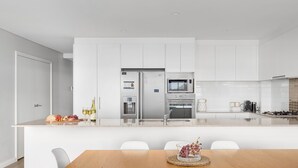 Eine moderne Küche mit weißen Schränken, einem Edelstahlkühlschrank, einer Mikrowelle und einem Backofen. Ein Esstisch mit Stühlen und einer Traubenkranz-Dekoration steht ebenfalls bereit.