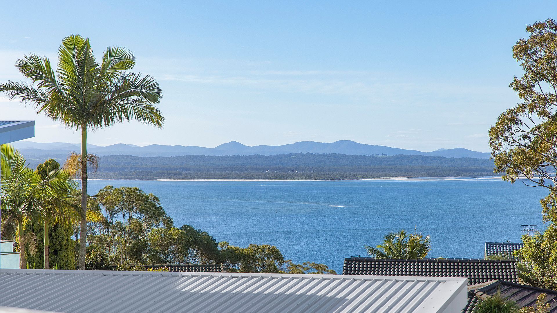 A coastal view with a clear sky, a beach, and distant mountains.