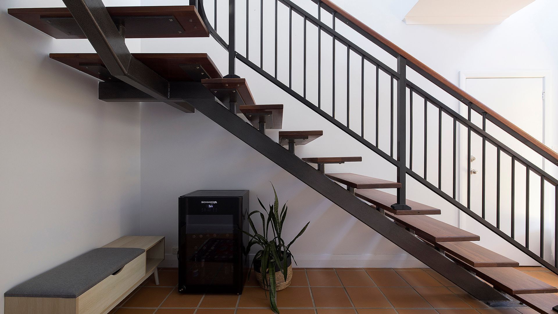 A staircase with wooden steps and metal railings, a bench, a black electronic device, and a potted plant.