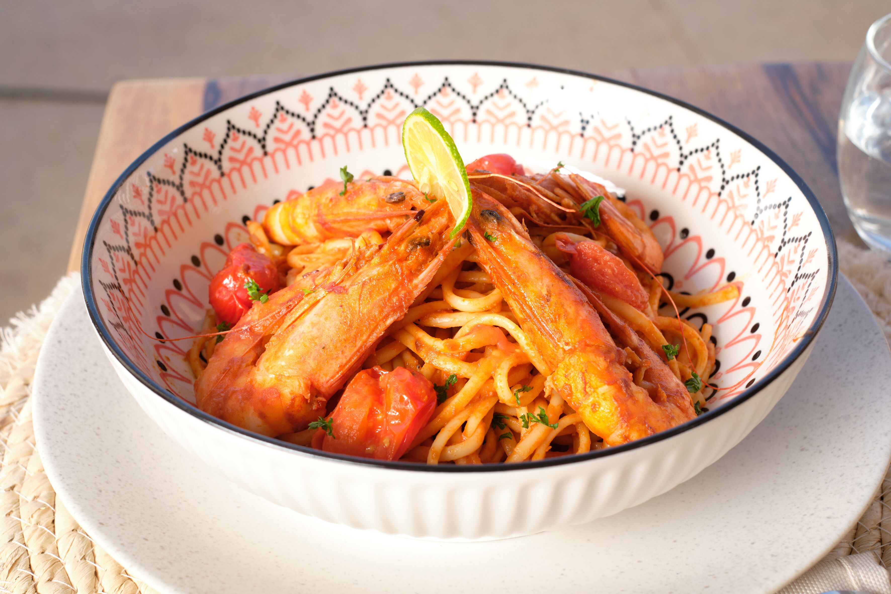 A bowl of pasta with shrimp and tomatoes, garnished with a lime wedge.