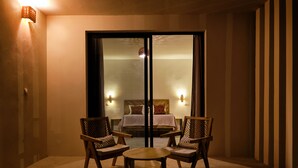 A room with a bed, two chairs, a table, and a sliding glass door leading to a bedroom. - Kawga Hôtel  (Ngaring)