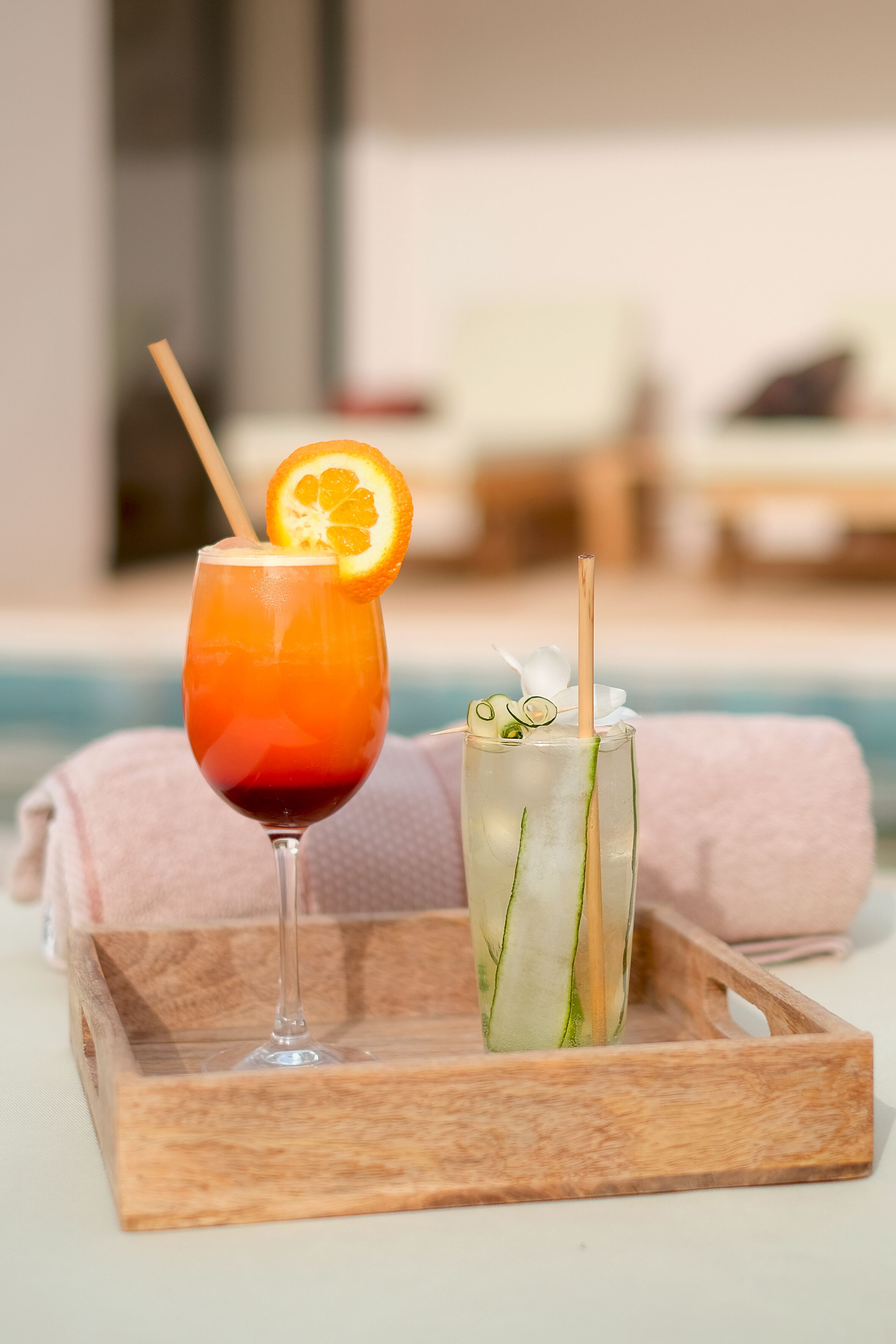 Dos bebidas sobre una bandeja de madera junto a una piscina.