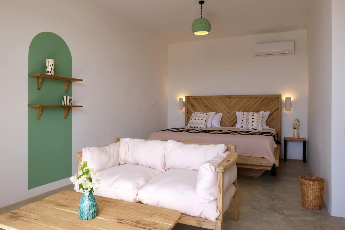 A bedroom with a bed, a sofa, a wooden table, a vase with flowers, and a green wall.
