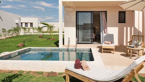 A modern outdoor pool area with a lounge chair, a small table, and a glass-enclosed room. - Kawga Hôtel  (Ngaring)