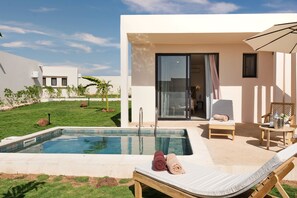 A modern outdoor pool area with a lounge chair, a small table, and a glass-enclosed room. - Kawga Hôtel  (Ngaring)