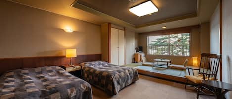 A hotel room with two beds, a desk, a chair, a small table, a window with a view, and a lamp.