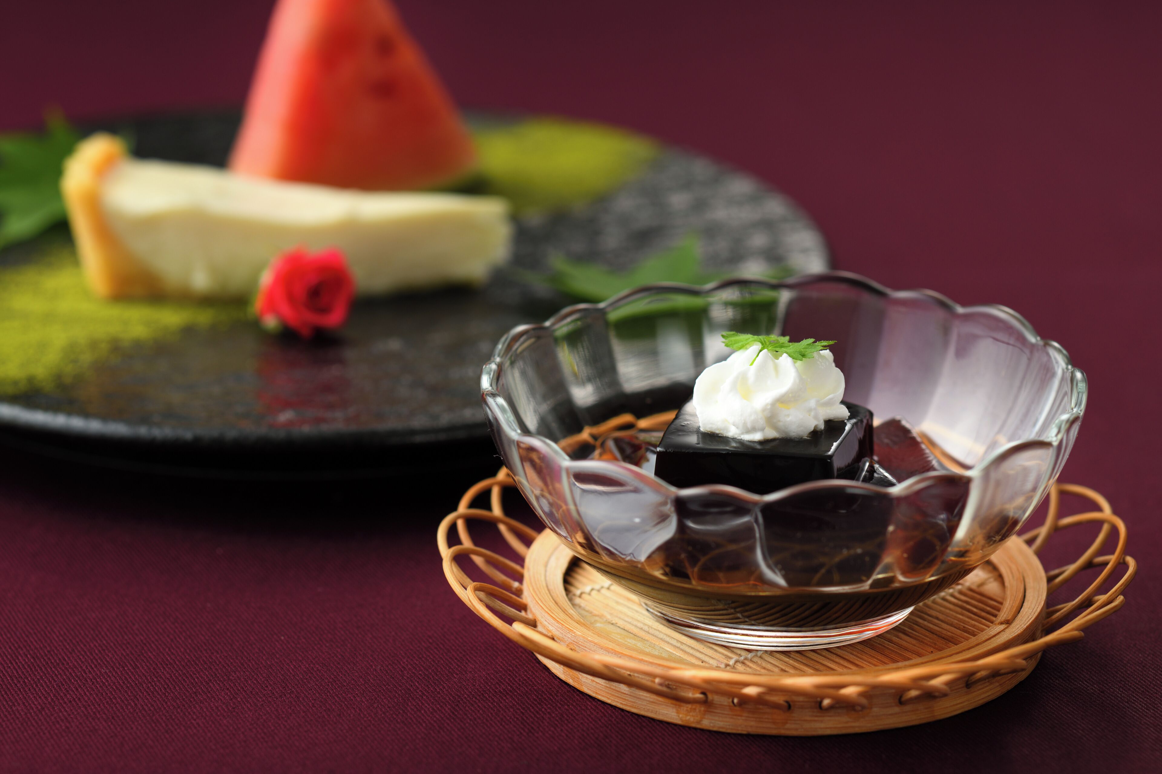 Une assiette à dessert avec une pastèque, une rose et un bol de dessert au chocolat, le tout posé sur un tapis tressé.