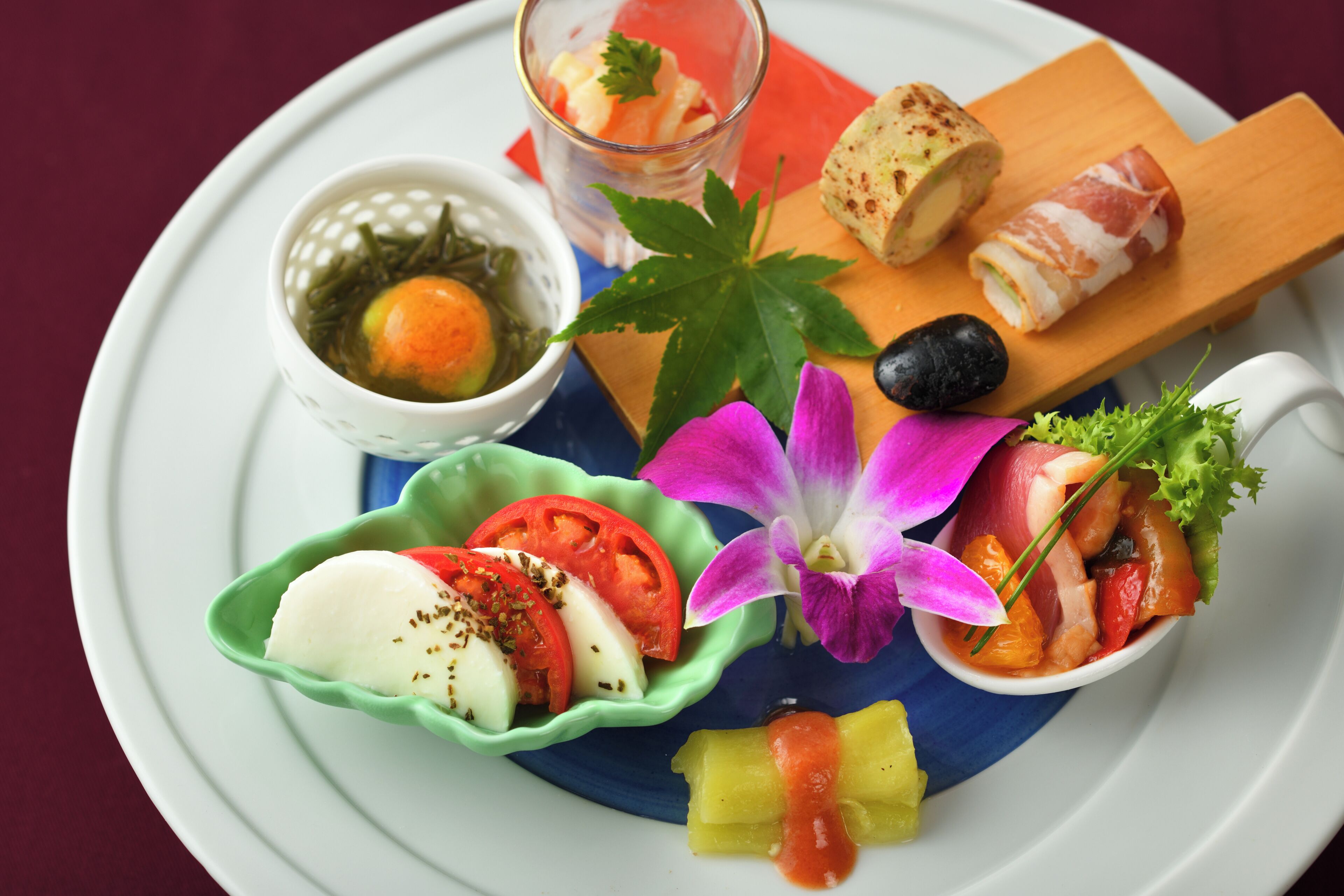 A plate with various food items including a boiled egg, a slice of tomato, a piece of cheese, and a small bowl of sauce.
