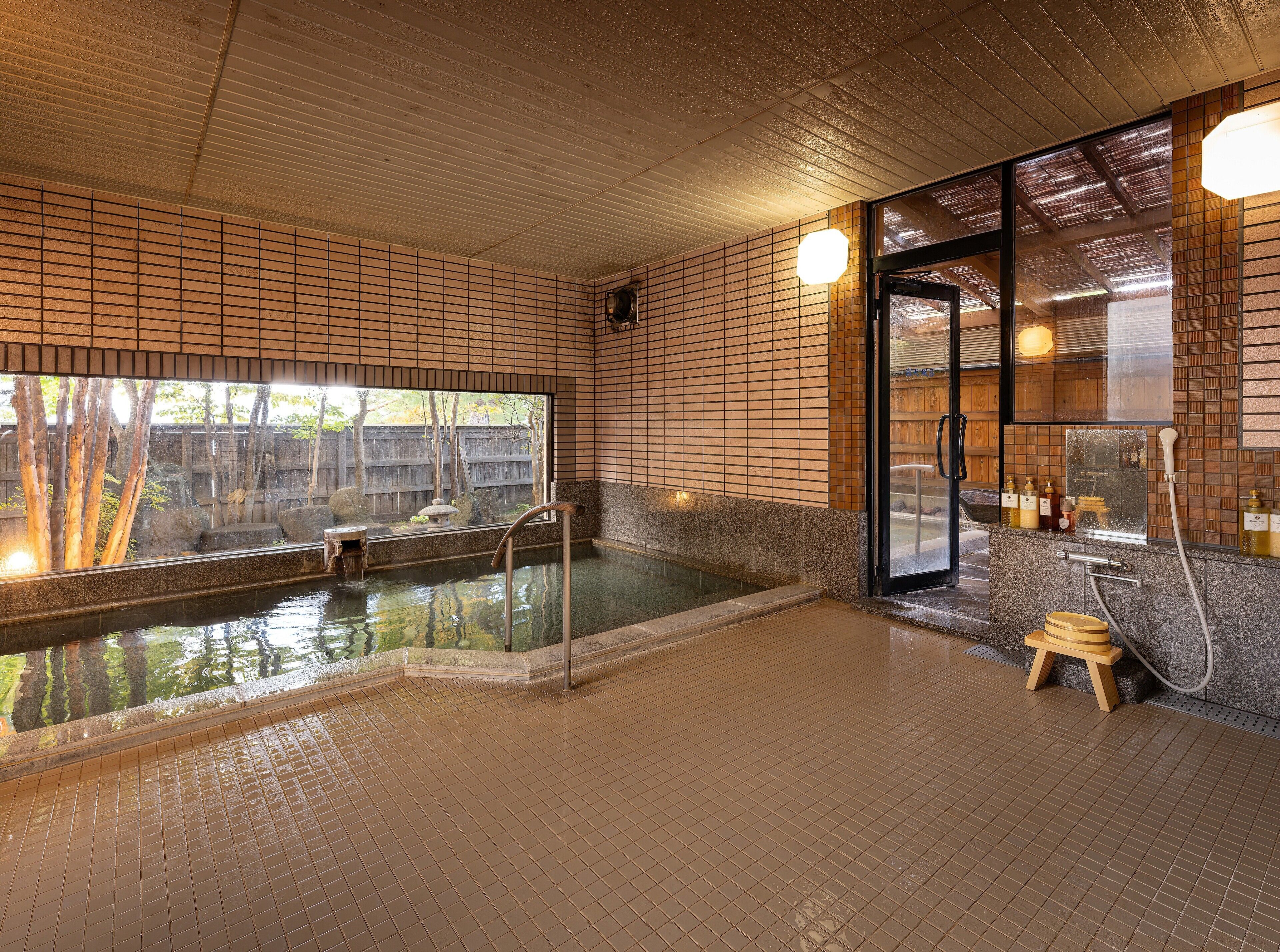 Uma onsen japonesa tradicional com um deck de madeira, um banquinho de madeira pequeno e uma nascente termal com cobertura de vidro.