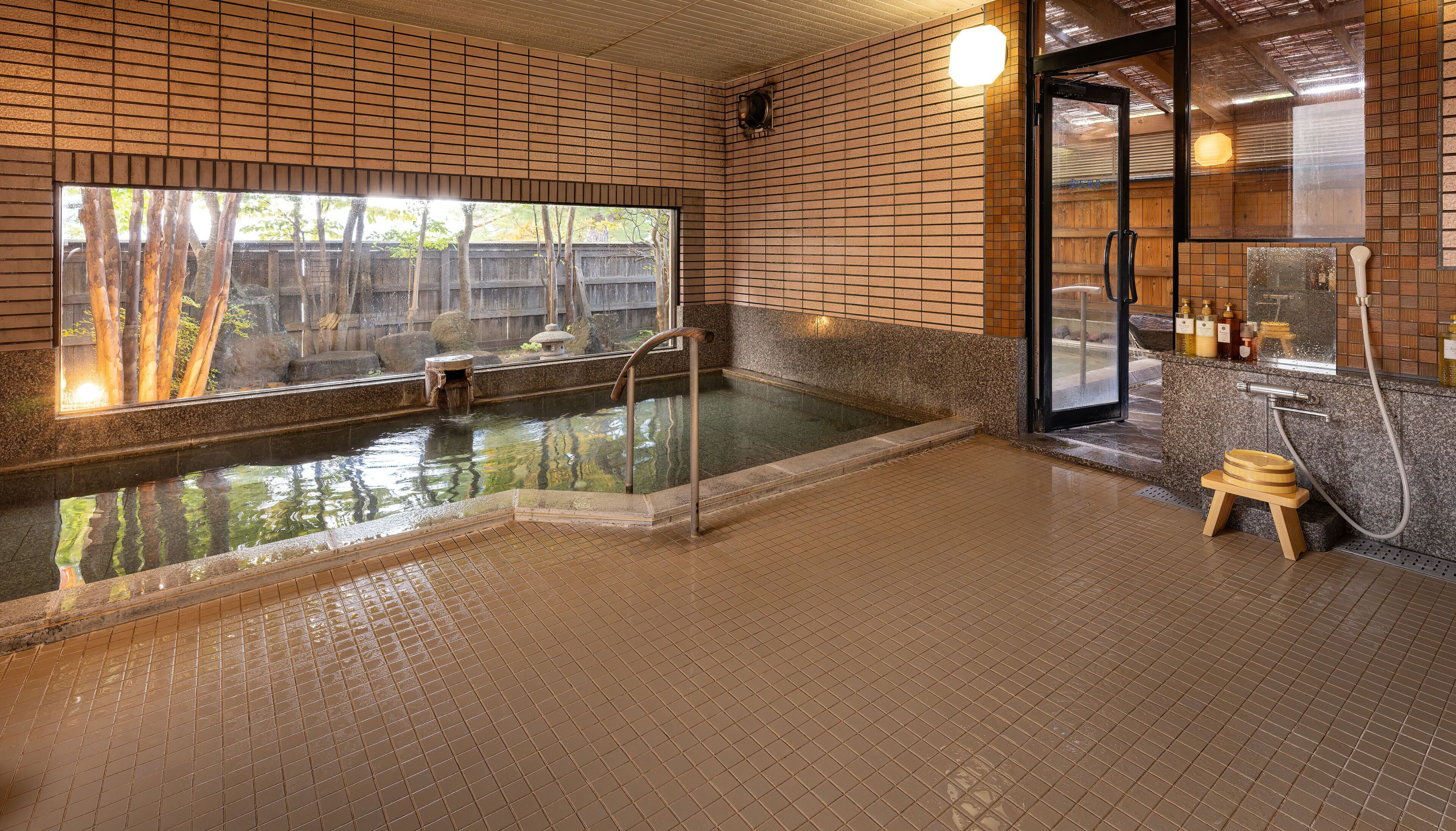Un espacio de spa con una bañera de hidromasaje, un taburete de madera y una puerta de cristal que da a la zona de ducha.