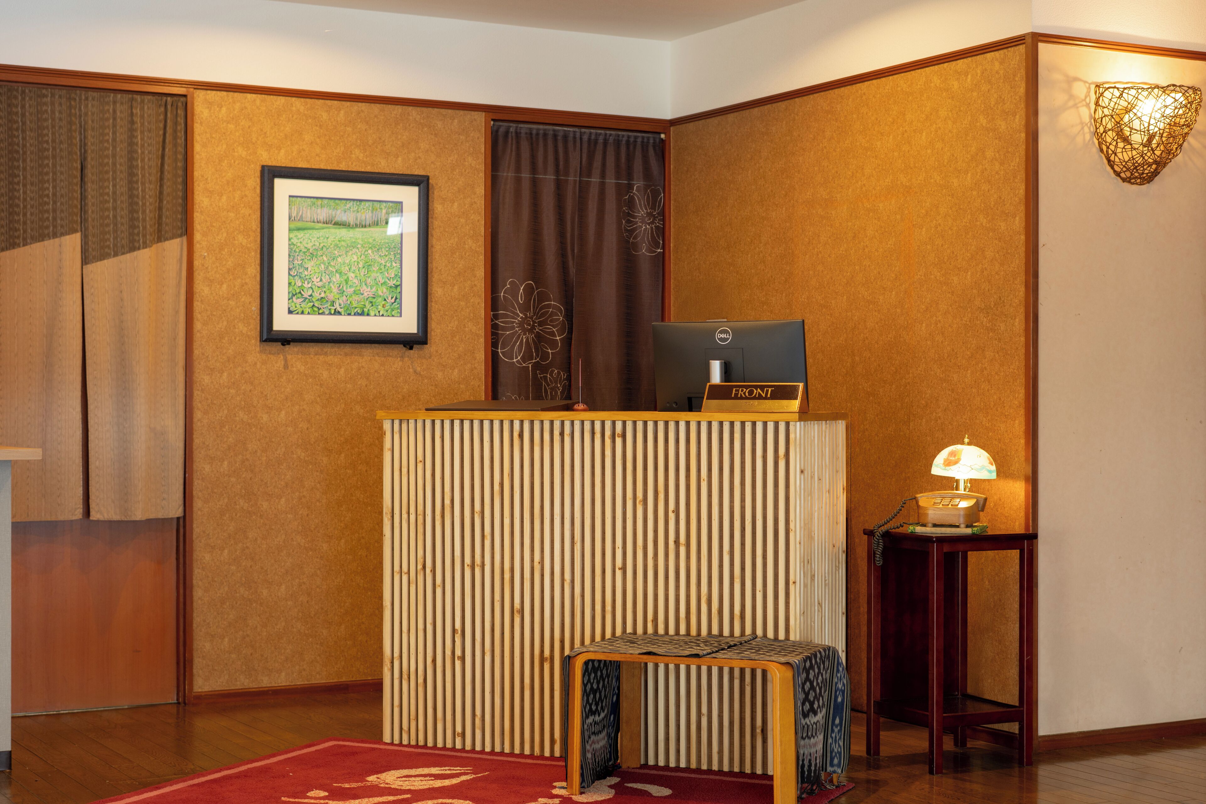 A reception desk with a computer, a small table with a lamp, and a framed picture on the wall.