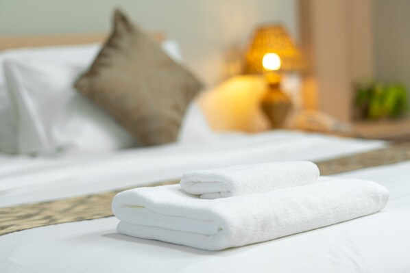 A neatly made bed with white linens and a folded towel on top.