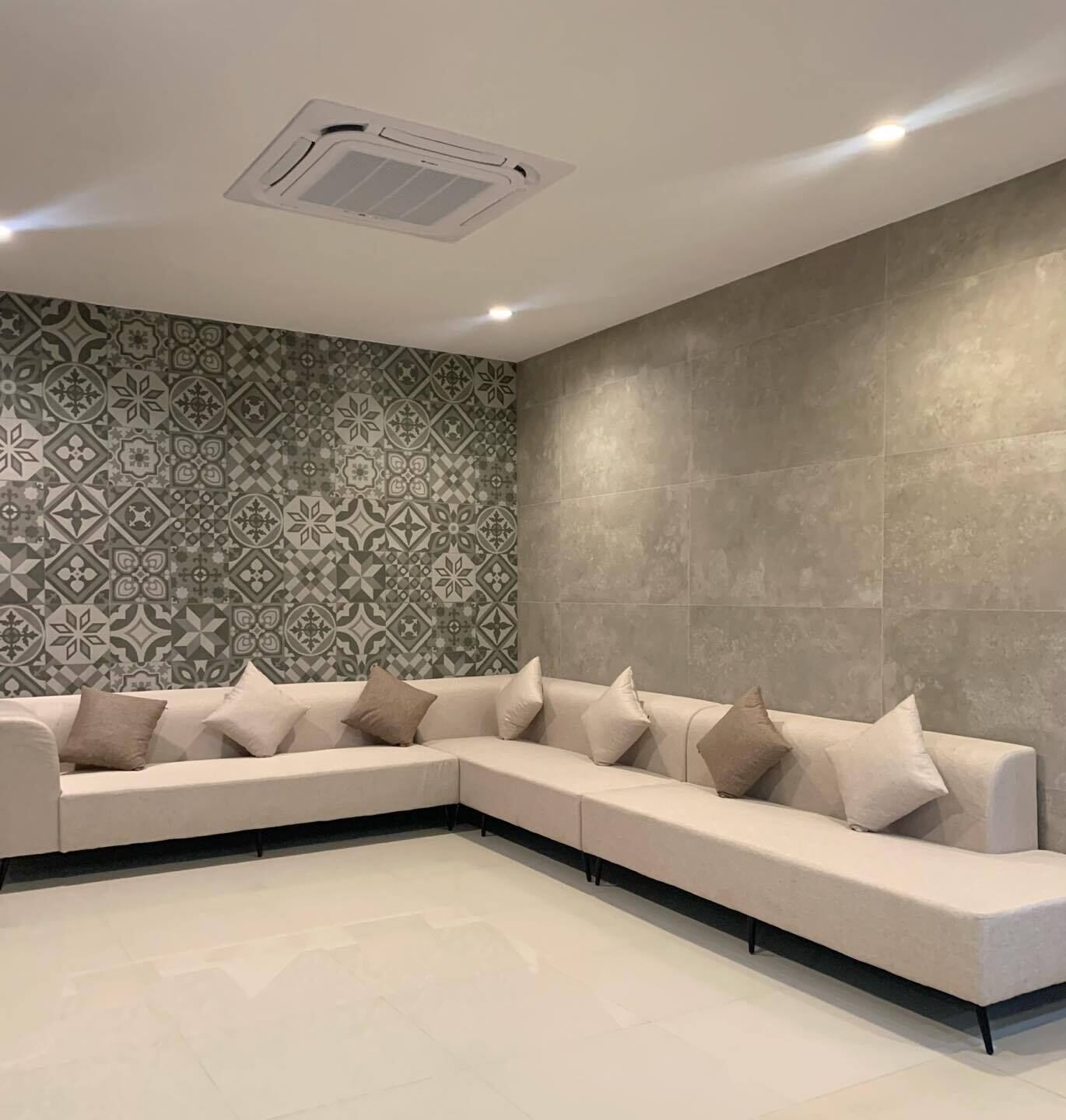 A modern living room with a beige sectional sofa, patterned wallpaper, and a recessed ceiling light.