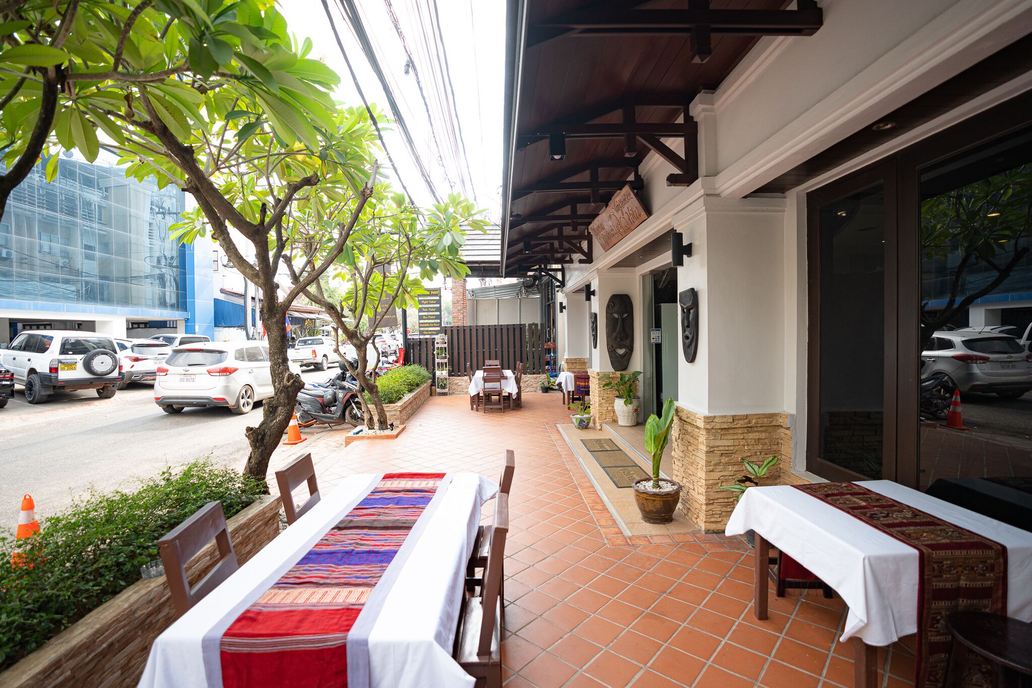 An outdoor dining area with a table set for two, a potted plant, and a view of the street.