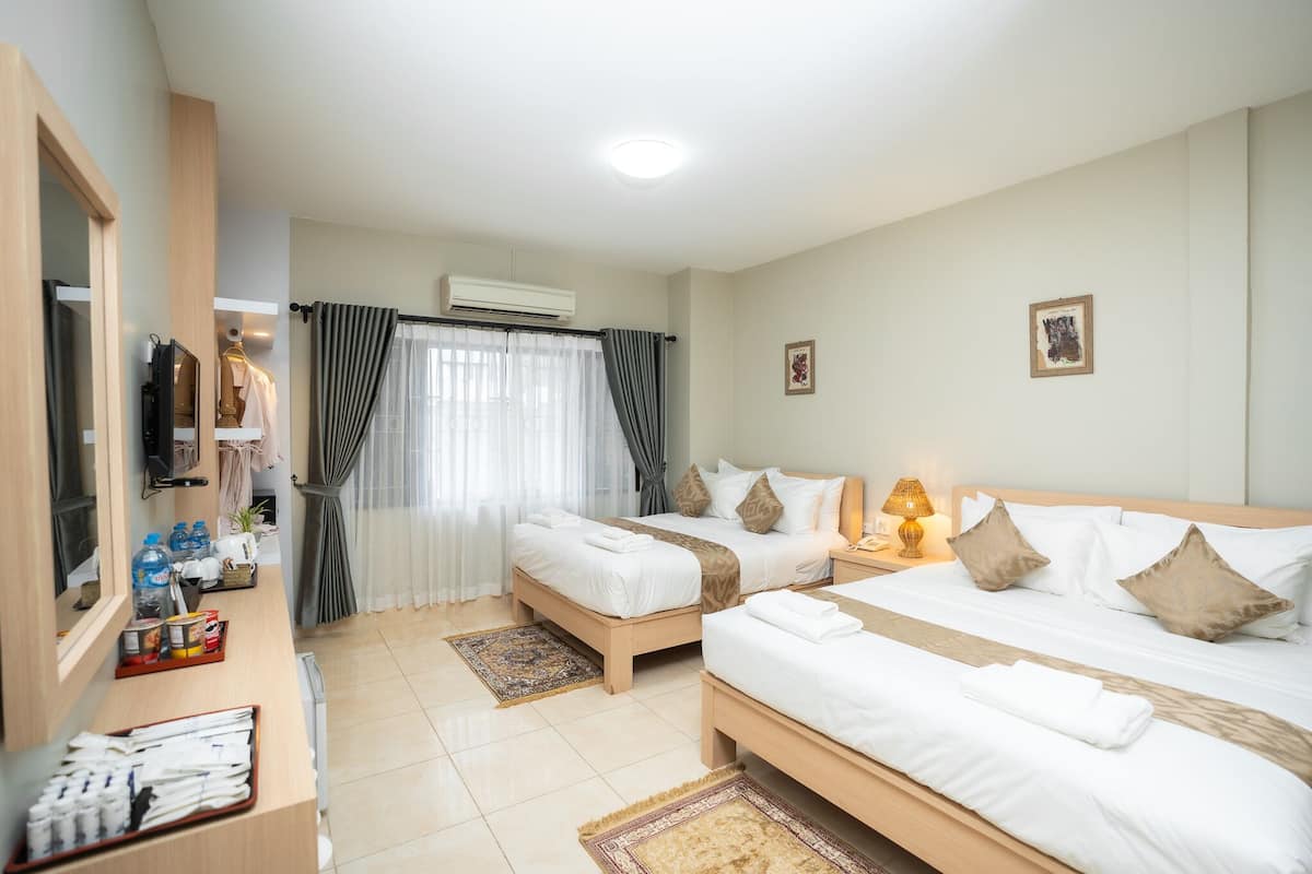A hotel room with two beds, a desk with toiletries, a TV, and an air conditioning unit.