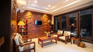 A modern living room with a wooden wall, a flat-screen TV, a sofa, a coffee table, and a large window with a view. - Vongkhamsene Boutique Hotel (Vientiane)