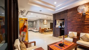 A hotel lobby with a sofa, coffee table, and fan. There is a wooden wall and a tiled floor. - Vongkhamsene Boutique Hotel (Vientiane)