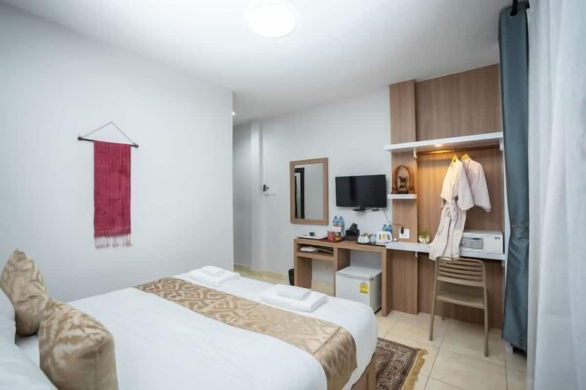 A hotel room with a bed, a desk with a computer, a TV, and a mirror.