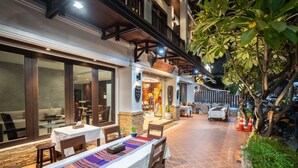 An outdoor dining area with tables and chairs, a stone wall, and a staircase leading to an upper level. - Vongkhamsene Boutique Hotel (Vientiane)