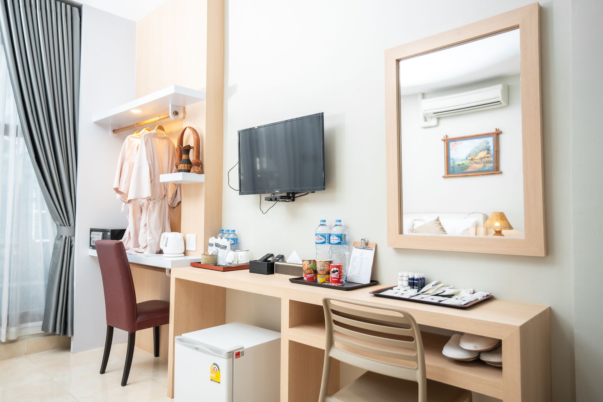 A hotel room with a desk, chairs, a television, a mini-fridge, and a bed.