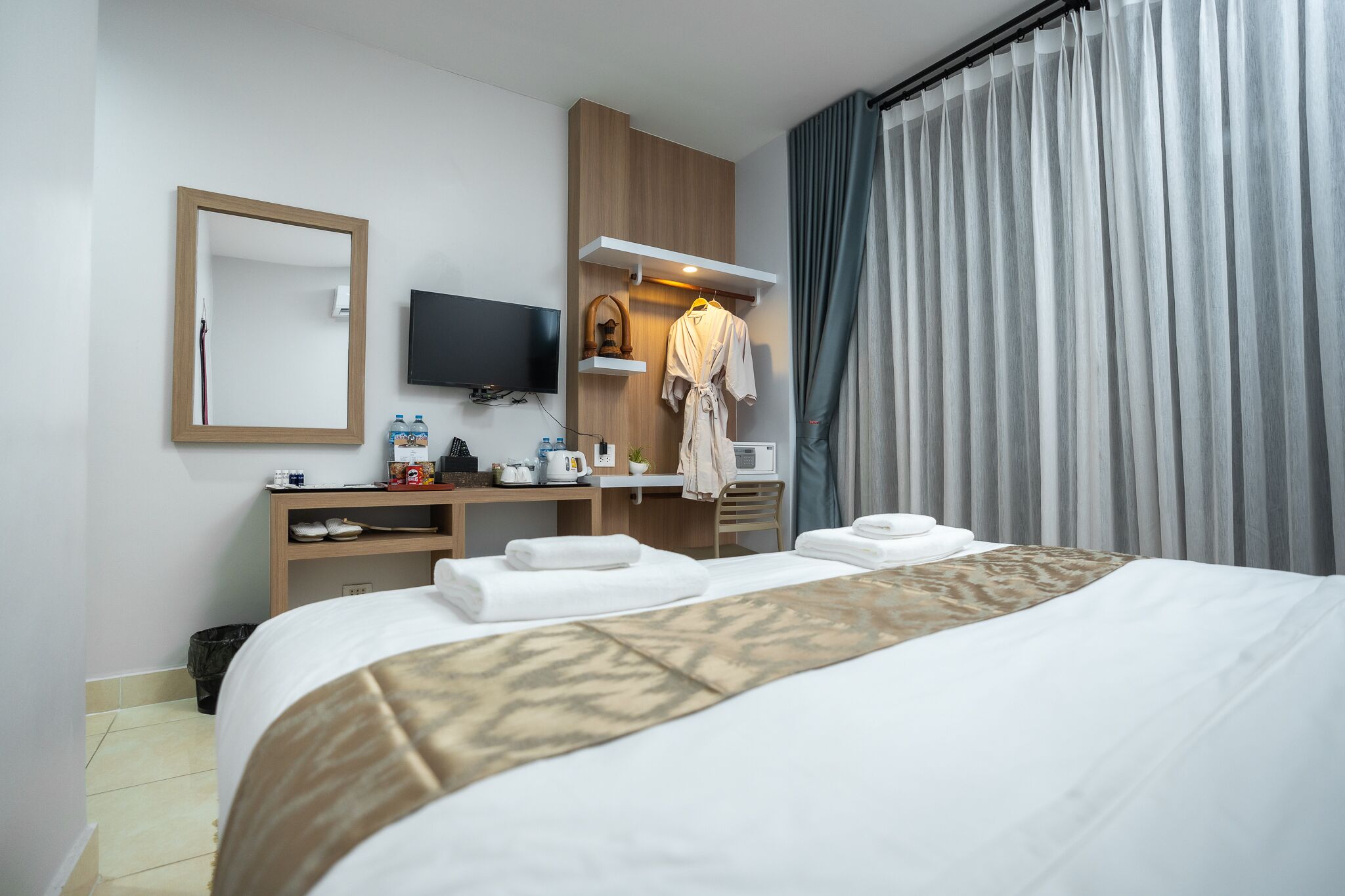 A hotel room with a bed, a desk with a flat-screen TV, a robe, and a shower area.