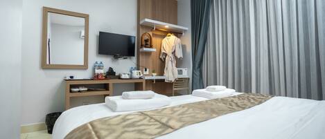 A hotel room with a bed, a desk with a flat-screen TV, a robe, and a shower area.