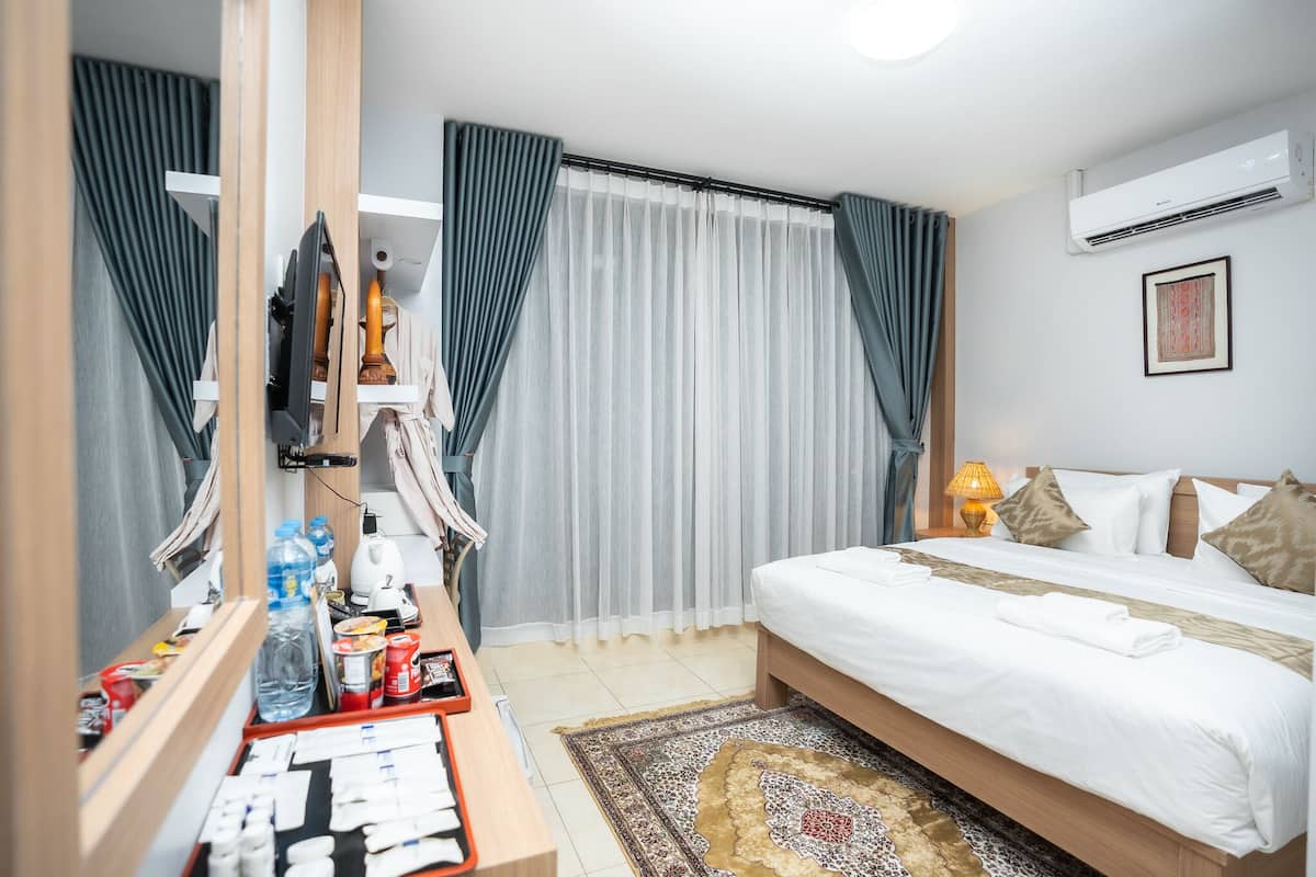 A hotel room with a bed, bedside table, mirror, curtains, and an air conditioning unit.