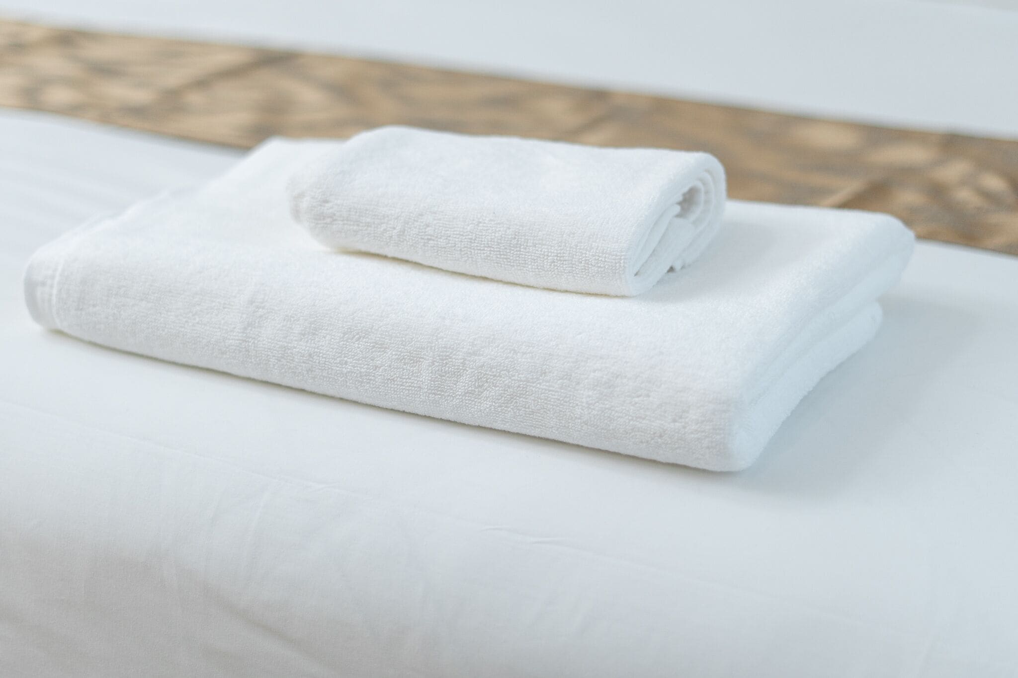 Una toalla blanca doblada cuidadosamente sobre una cama blanca en una habitación con suelo de madera.