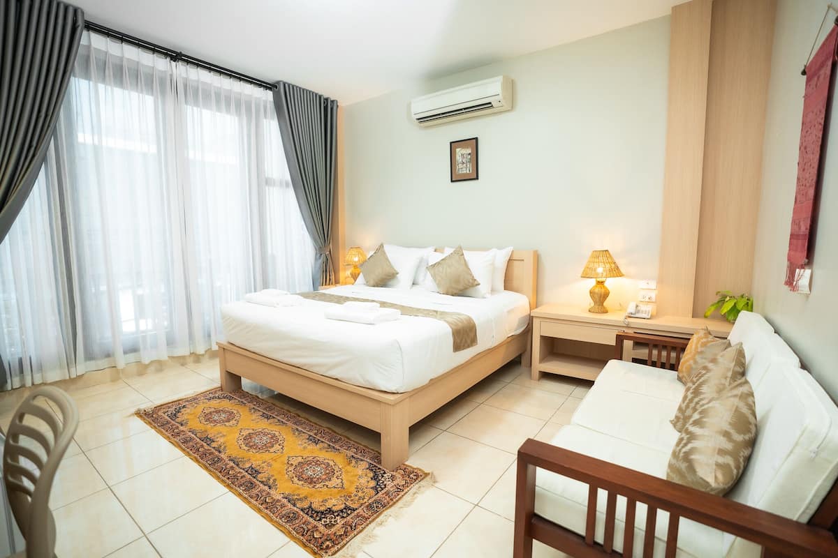 A hotel room with a bed, bedside table, lamp, and a small sofa.