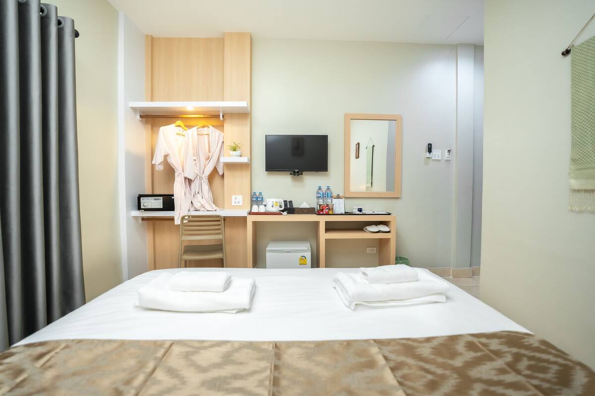 A hotel room with a bed, a desk with a TV, a robe, and toiletries.