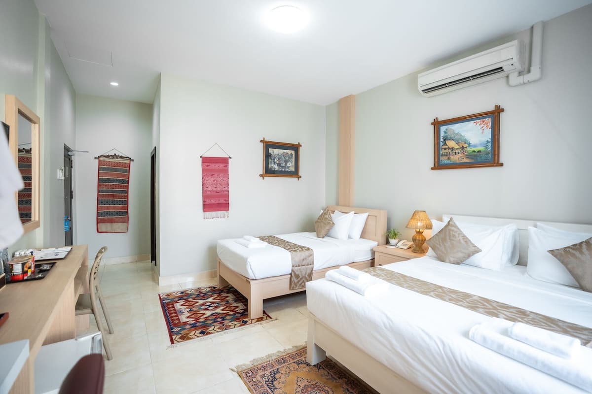 A hotel room with two beds, a desk, and a chair. There is a desk lamp, a wall-mounted air conditioner, and a framed picture on the wall.
