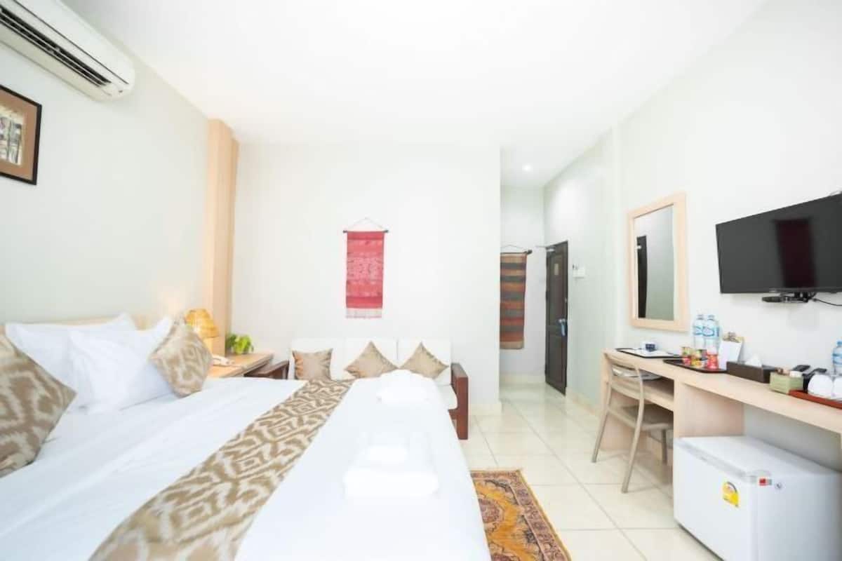 A hotel room with a bed, desk, TV, and a small refrigerator.