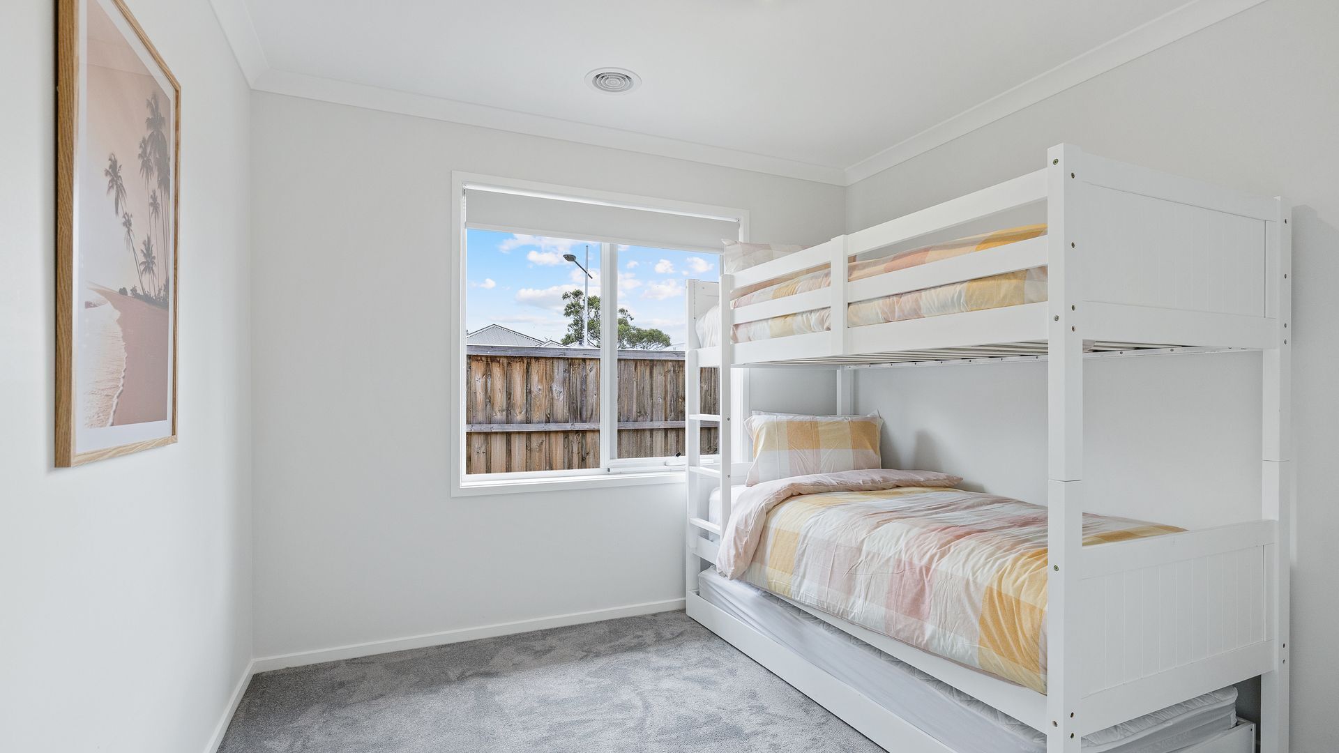 A bedroom with a bunk bed, a window with a view of a wooden fence, and a framed picture on the wall.