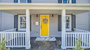 A two-story house with a bright yellow front door, white railings, and a covered porch.