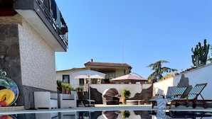 A clear swimming pool with lounge chairs and umbrellas, a stone wall, and a building with a tiled roof in the background. - villa Elisabetta (Pompei)