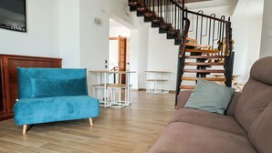 A living room with a blue sofa, a brown sofa, a wooden staircase, and a dining area with white tables. - villa Elisabetta (Pompei)