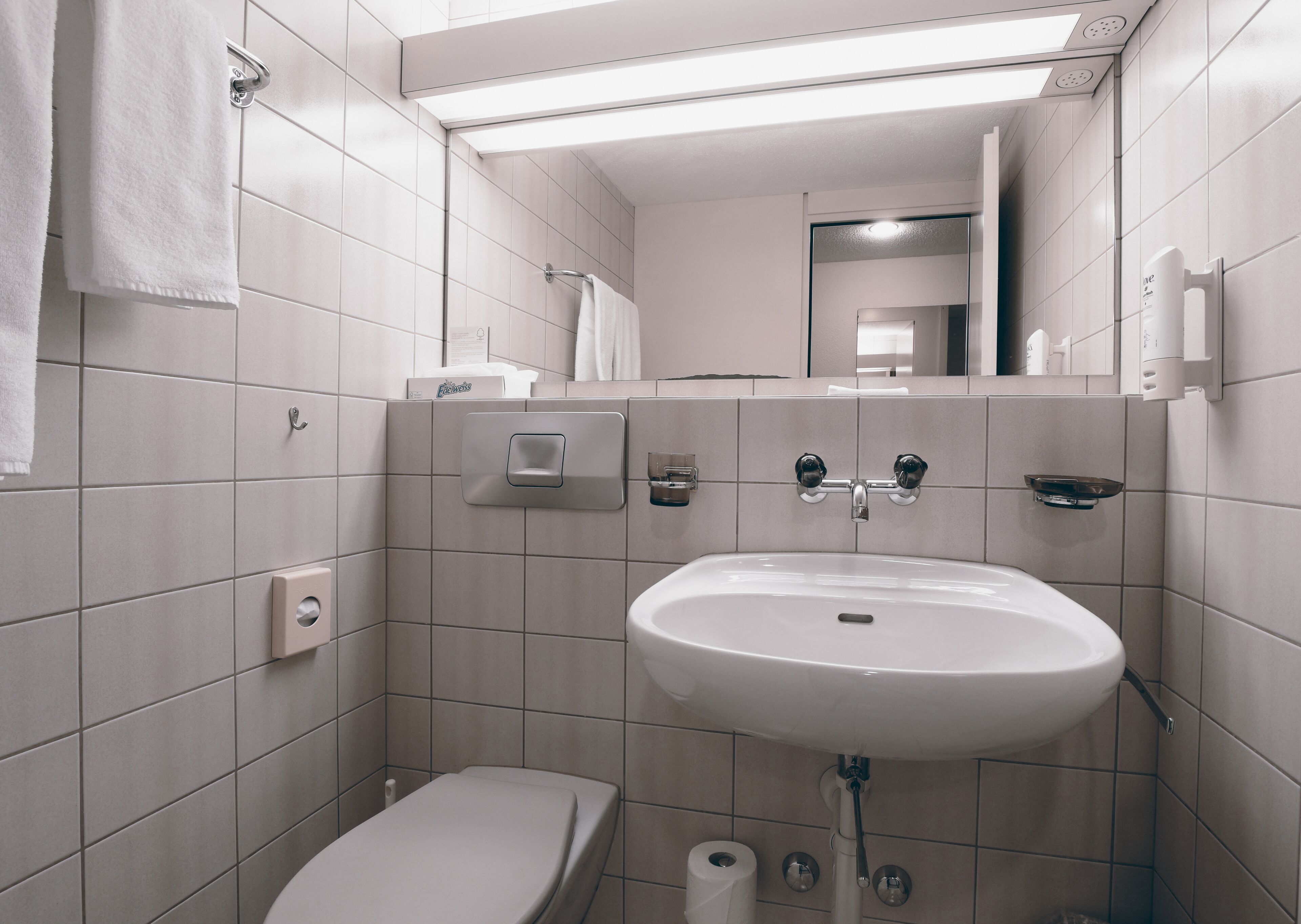 Un baño moderno con lavamanos, inodoro y toallero blancos.