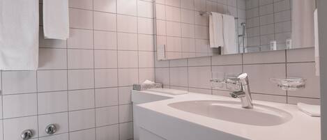 Un baño moderno con baldosas blancas, inodoro, lavabo con espejo y un perchero para toallas.