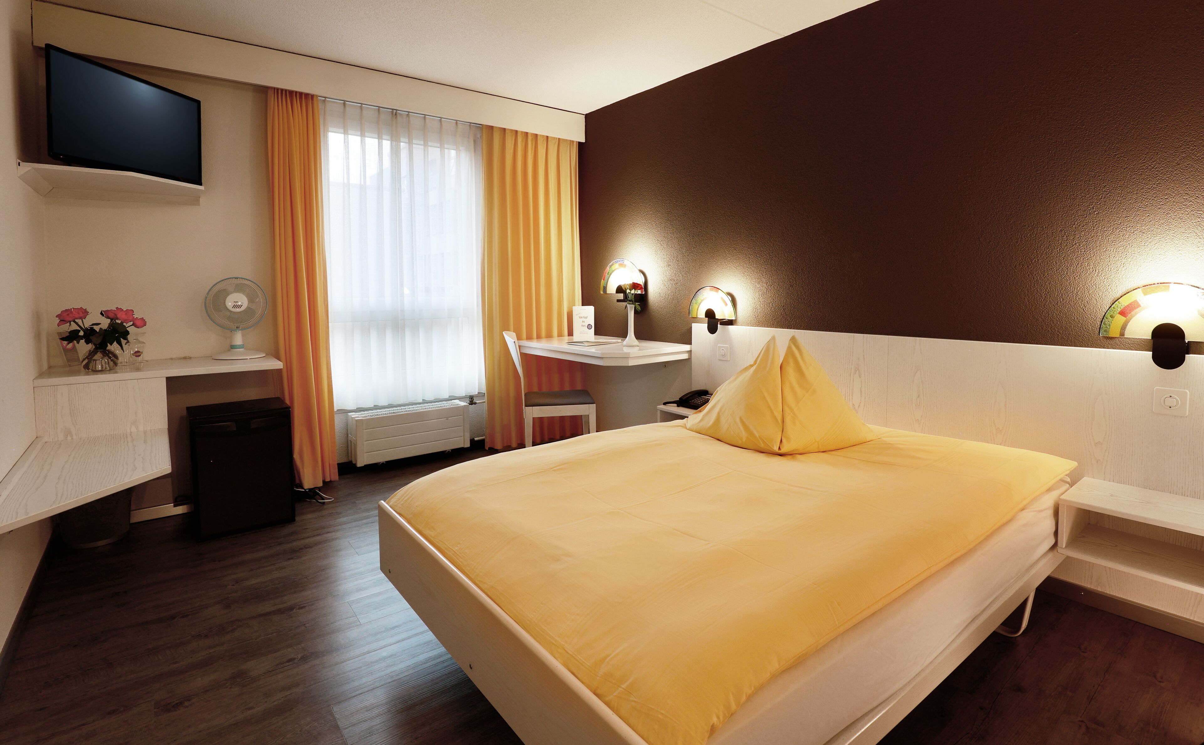 A hotel room with a bed, desk, chair, and a TV mounted on the wall.
