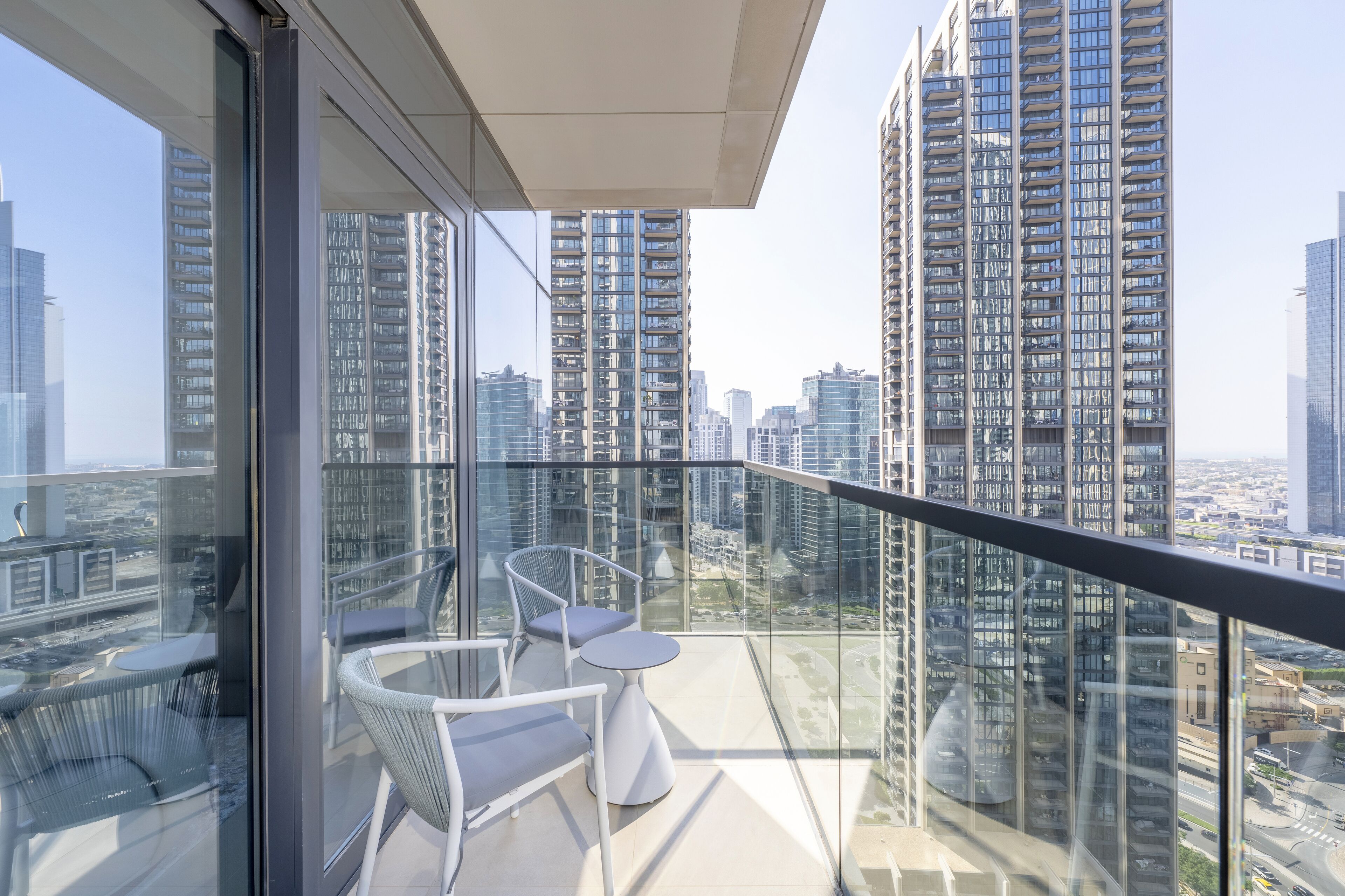 Un balcon doté de balustrades en verre, de chaises blanches et d’une petite table.