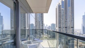 Ein Balkon mit Glasgeländern, weißen Stühlen und einem kleinen Tisch.