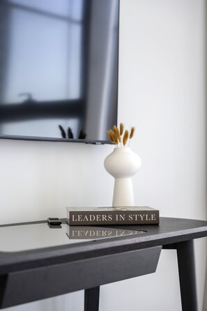 A modern desk with a book titled "LEADERS IN STYLE" and a white vase with dried plants.